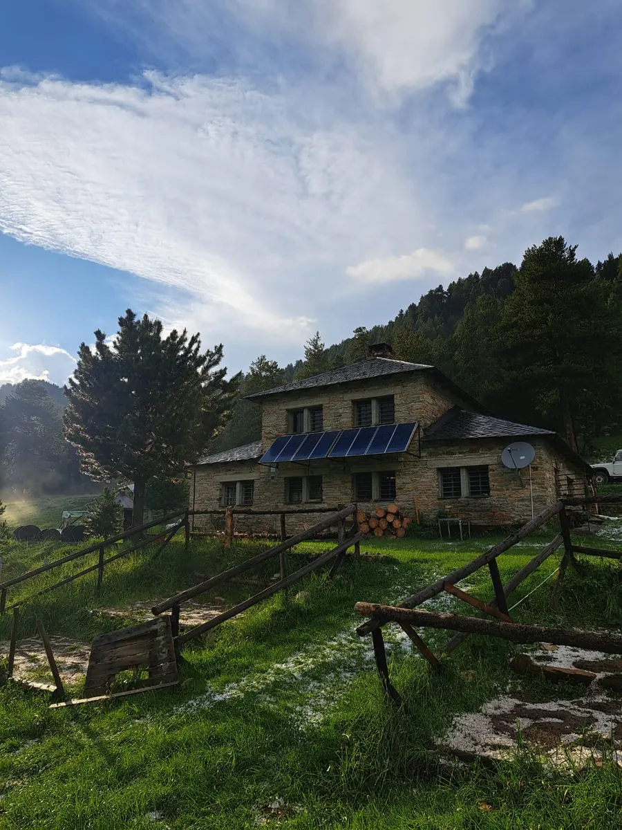 Casa de montaña de piedra con jardín y entorno verde.